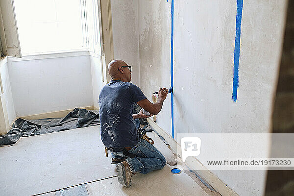 Bald construction worker painting on wall