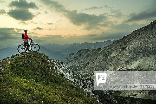 Biker with bicycle on top of mountain under cloudy sky
