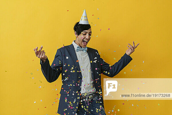 Joyful young man with party hat throwing confetti in studio