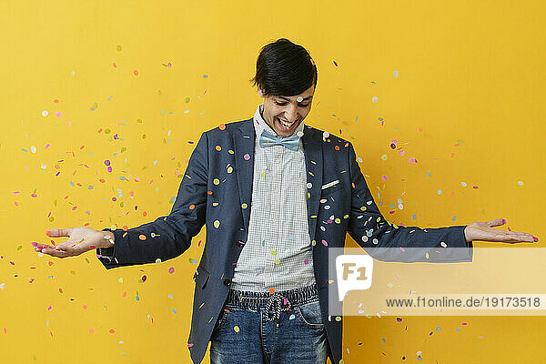 Happy man playing with confetti against yellow background