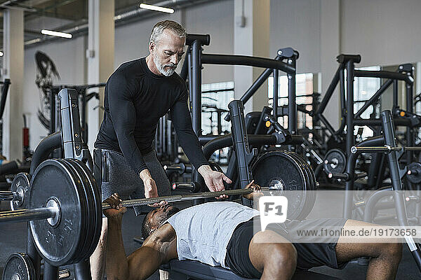 Fitness instructor helping young man with bench press in gym