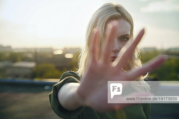 Serious blond woman showing stop gesture at sunset
