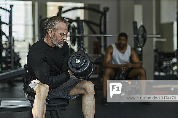 Mature man exercising with man in background at gym