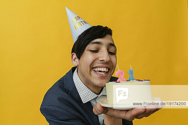 Joyful young man with party hat looking at birthday cake