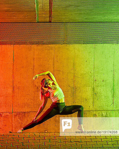Active woman doing yoga near neon colored wall