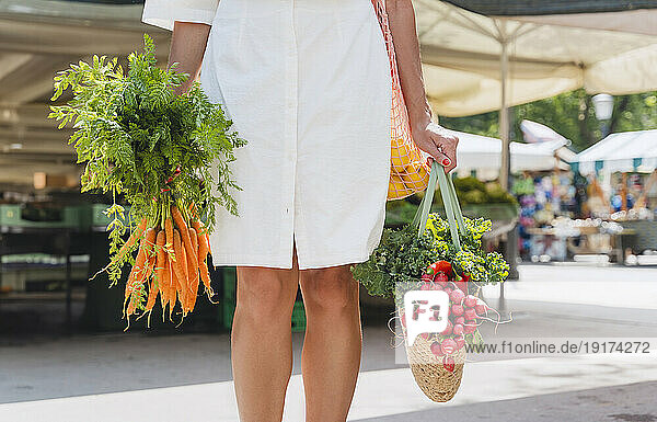 Hands of woman holding bag of groceries and bunch of carrots