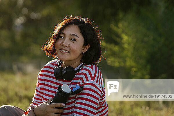 Smiling woman with water bottle and headphones in field