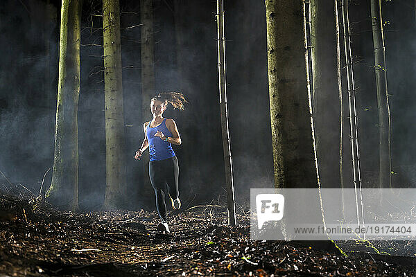 Determined young sportswoman running in forest during foggy weather