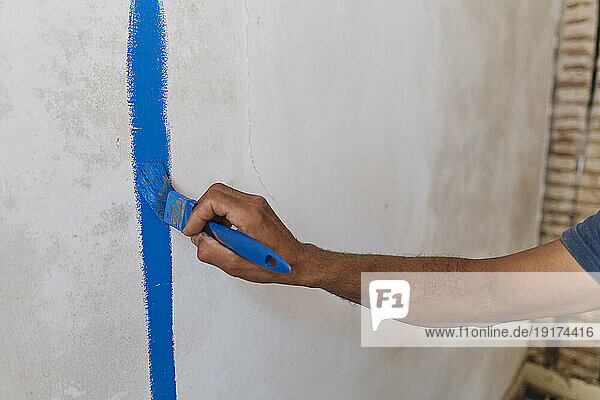 Hand of construction worker applying blue paint on wall