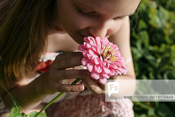 Girl holding and smelling pink flower in garden