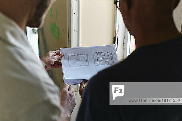 Architect discussing over blue print with man at site