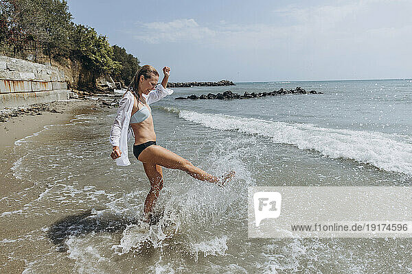 Playful woman splashing water with leg at beach