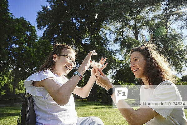 Smiling mother giving flower to daughter in park on sunny day