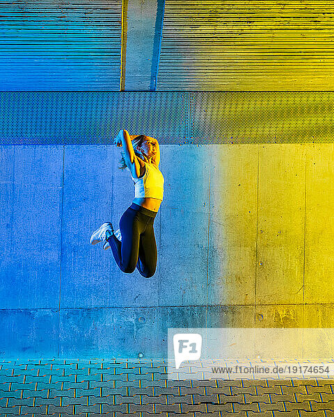 Active woman jumping in front of neon colored wall