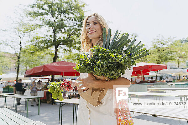 Happy woman holding fresh leafy vegetables in farmer's market