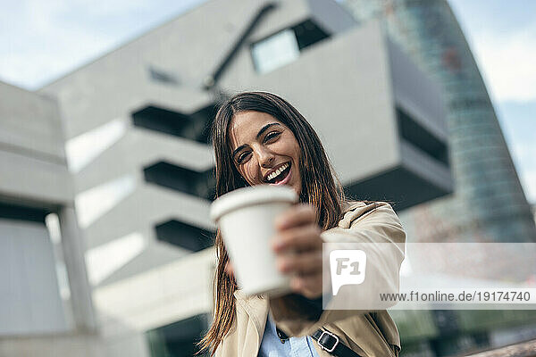 Happy young woman holding coffee cup in front of building