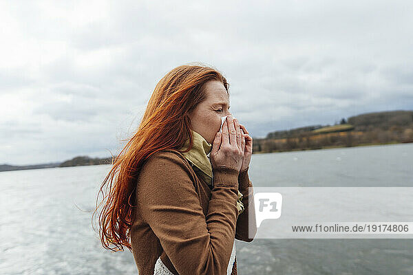 Redhead woman blowing nose by lake