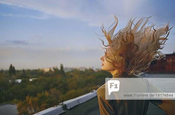 Carefree blond woman enjoying on rooftop at sunset