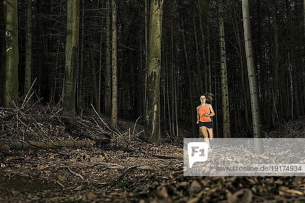 Dedicated sportswoman running amidst tree trunks in forest