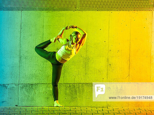 Woman doing yoga wearing sportswear in front of neon colored wall