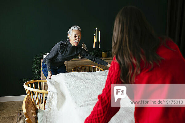 Mother and daughter placing tablecloth on dining table