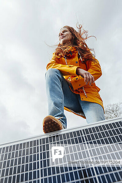 Redhead woman with leg on solar panel in front of sky