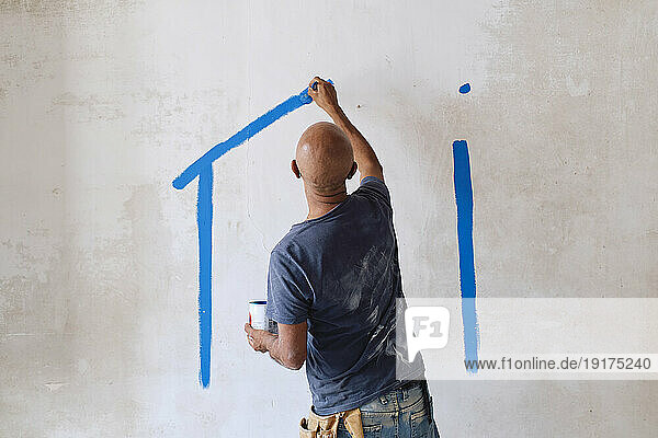 Bald construction worker drawing on wall with paintbrush at site