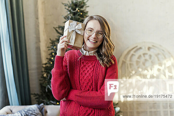 Happy woman wearing red sweater holding Christmas gift at home