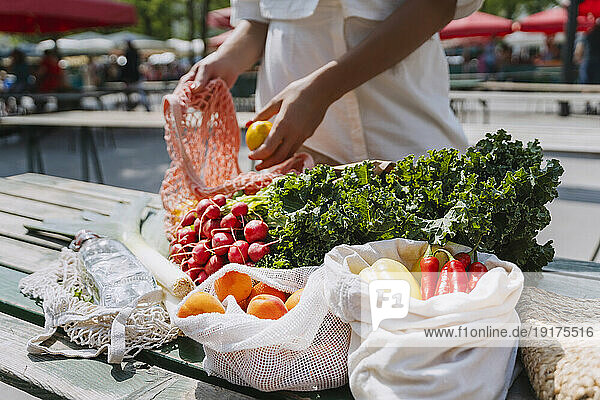 Woman buying fresh fruits and vegetables in market on sunny day