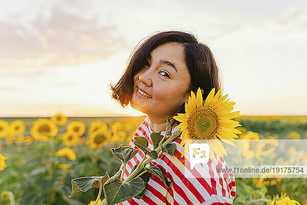 Mature smiling woman with sunflower at sunset