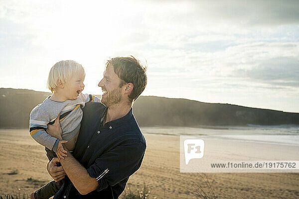 Cheerful father and son at beach on sunny day