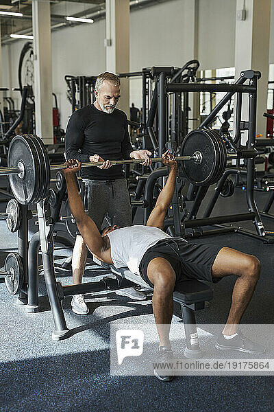 Mature trainer helping man for strength training in gym