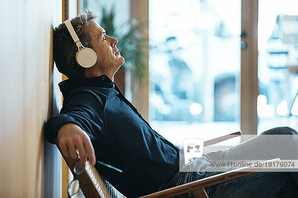 Mature man wearing wireless headphones sitting in armchair
