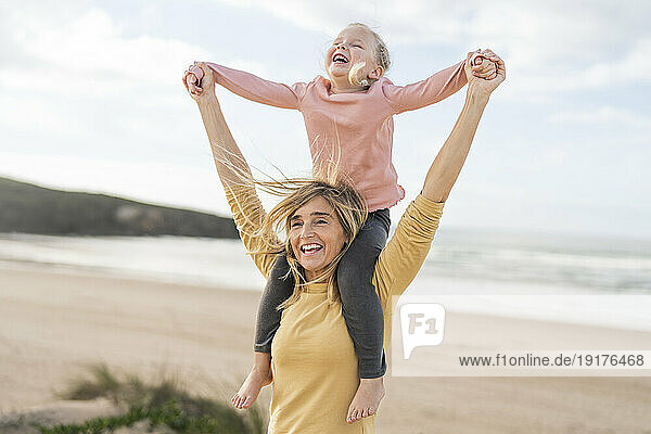 Happy mother carrying daughter on shoulders at beach