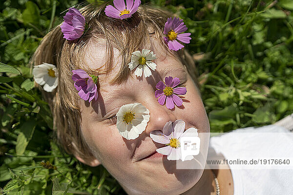 Smiling boy with flowers over face on sunny day