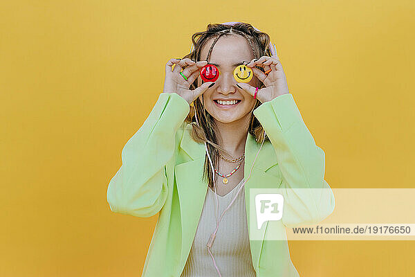 Smiling woman covering eyes with smileys against yellow background