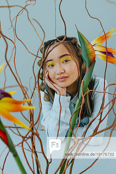Young woman with hand on chin seen through multi colored branches in studio