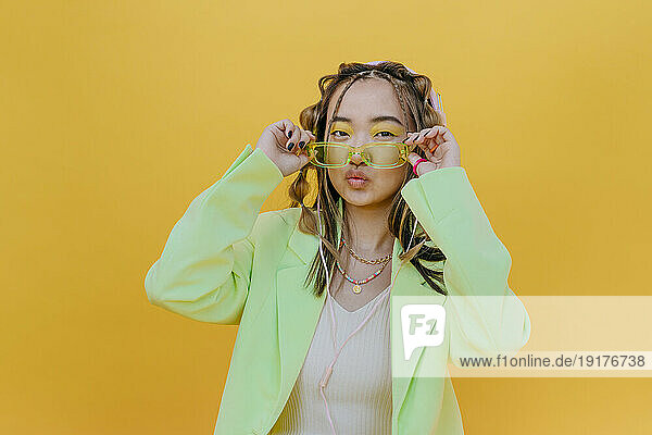 Young woman with sunglasses puckering against yellow background