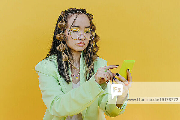 Young woman with sunglasses using mobile phone in studio