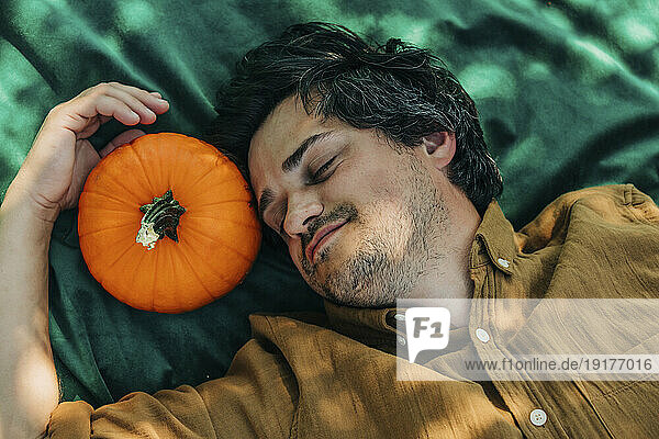 Smiling man lying near pumpkin on green blanket