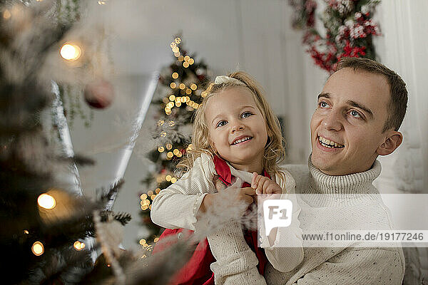 Happy father carrying daughter looking at christmas tree