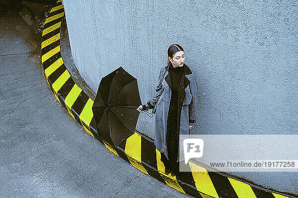 Woman holding umbrella leaning on wall