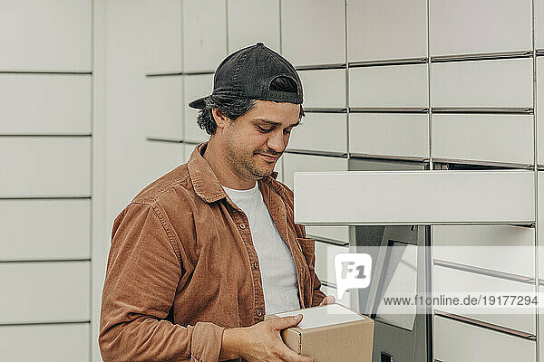 Smiling man wearing brown shirt holding delivery package near locker