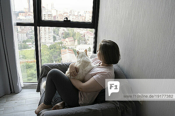 Thoughtful young woman sitting with cat on sofa at home