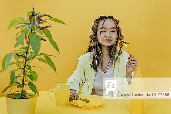 Young woman having pepper at table against yellow background