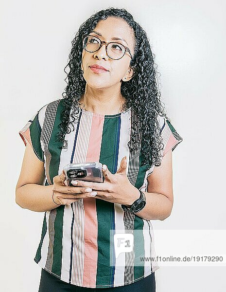 Nachdenkliche junge Frau mit Brille hält Handy isoliert. Nachdenklich lateinisches Mädchen hält Smartphone isoliert
