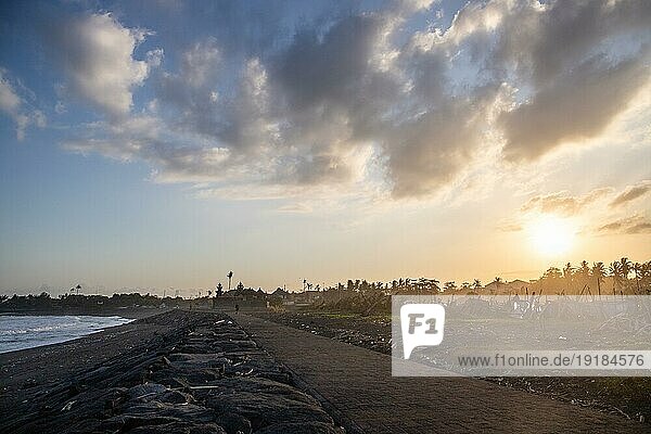 Schwarzer Sandstrand auf Bali  natürlich mit Tempeln  Booten (Jukung) und Wellen im Sonnenuntergang. Tropische Umgebung in Indonesien