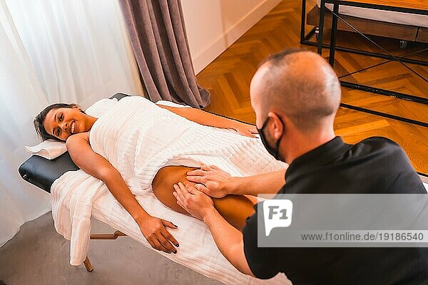 Massage zu Hause  Durchführung einer Massage zu Hause zufriedenen Kunden auf die Beine. Mit einer Gesichtsmaske in der Coronaviruspandemie