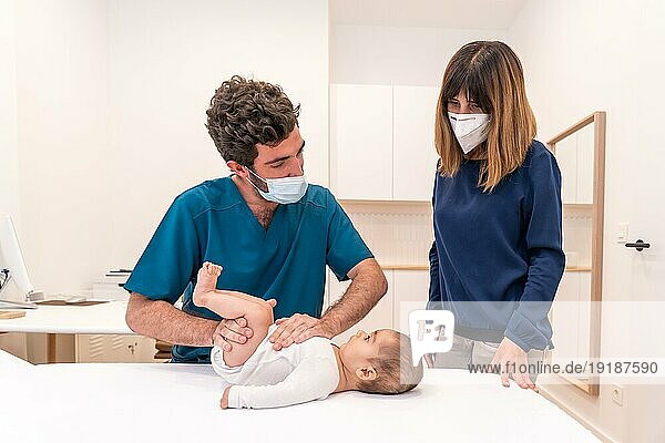 Frontalaufnahme eines jungen Arztes und einer Mutter bei einer Babyuntersuchung in einer Klinik