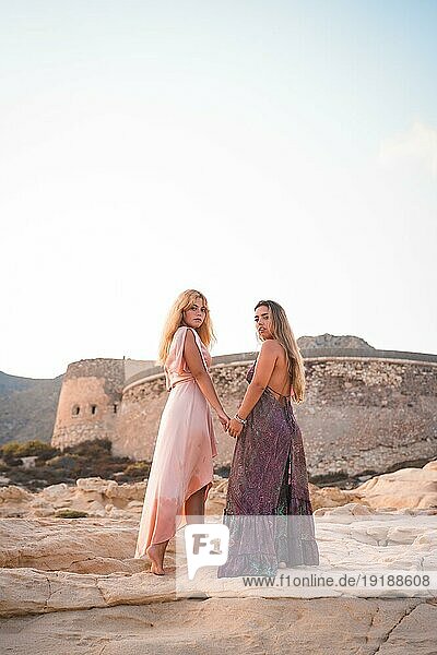 Ein paar kaukasische Mädchen mit rosa Kleidern  im Sommer am Playazo de Rodalquilar in Cabo de Gata neben der Burg im Sommer